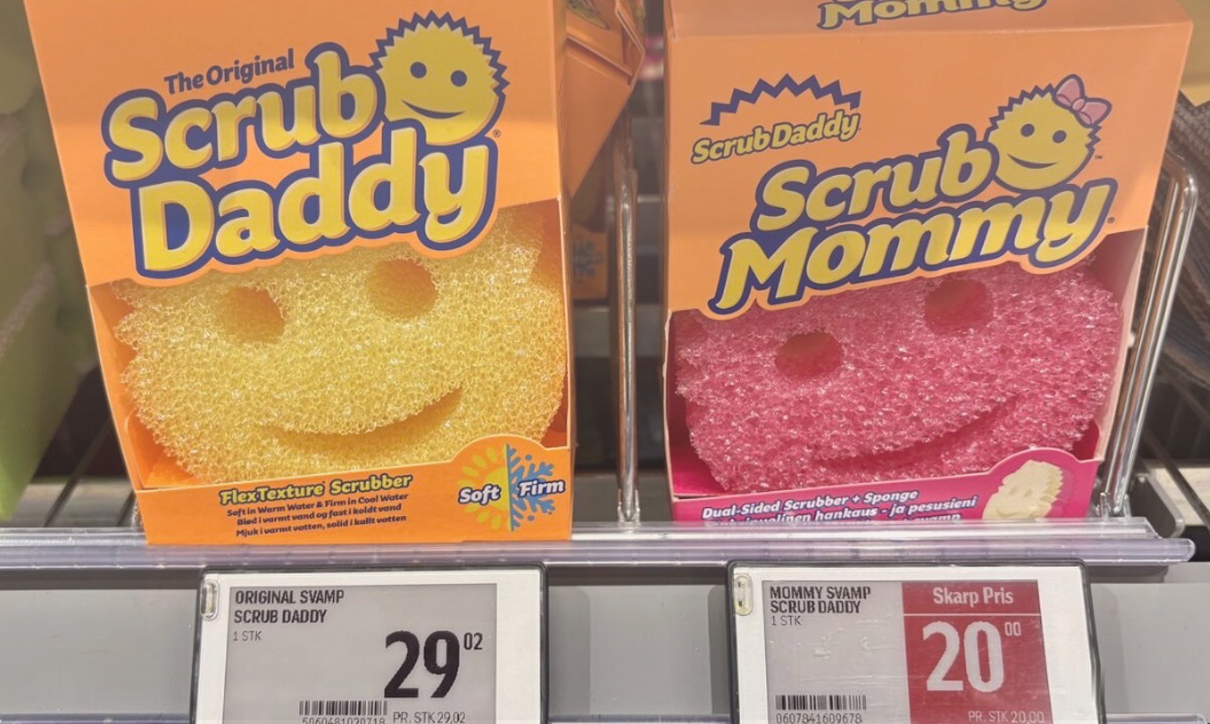 Photo of a retail shelf: the male-coded “Scrub Daddy” priced at 29.02 beside the female-coded “Scrub Mommy” at 20.00, sold as a variant of the same brand.