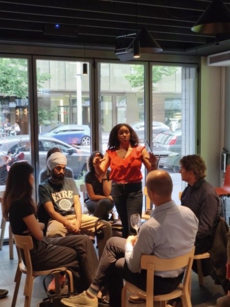 A speaker addressing a seated circle of participants by a window, working through how bias surfaces in AI-driven hiring.