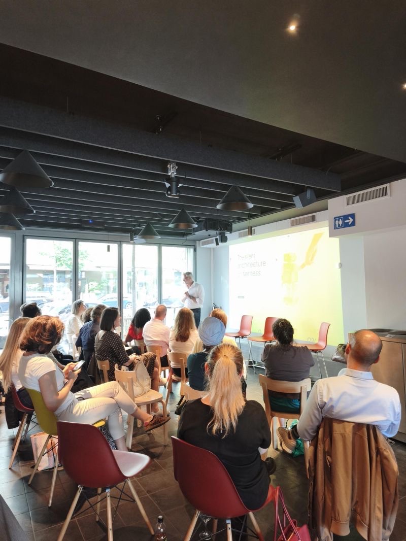 The full Trustworthy AI Circle room: an attentive audience seated in front of a speaker and a projected slide on the architecture of fairness.